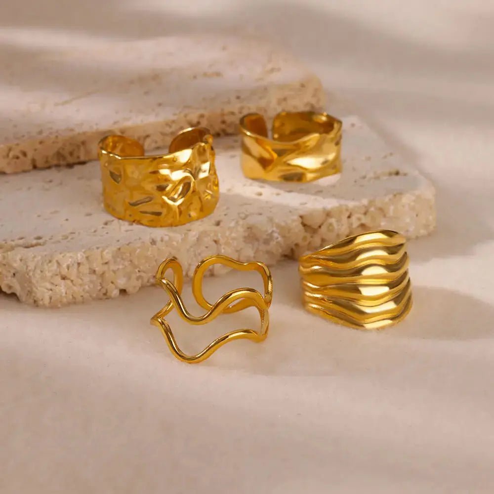 Irregular geometric gold ring collection showcasing chunky adjustable designs on a textured stone surface.